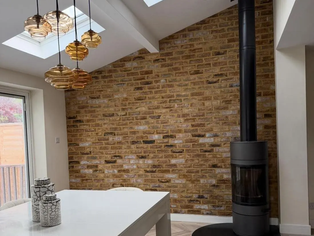 Warm brick slip wall beside a black wood burner in a kitchen dining room