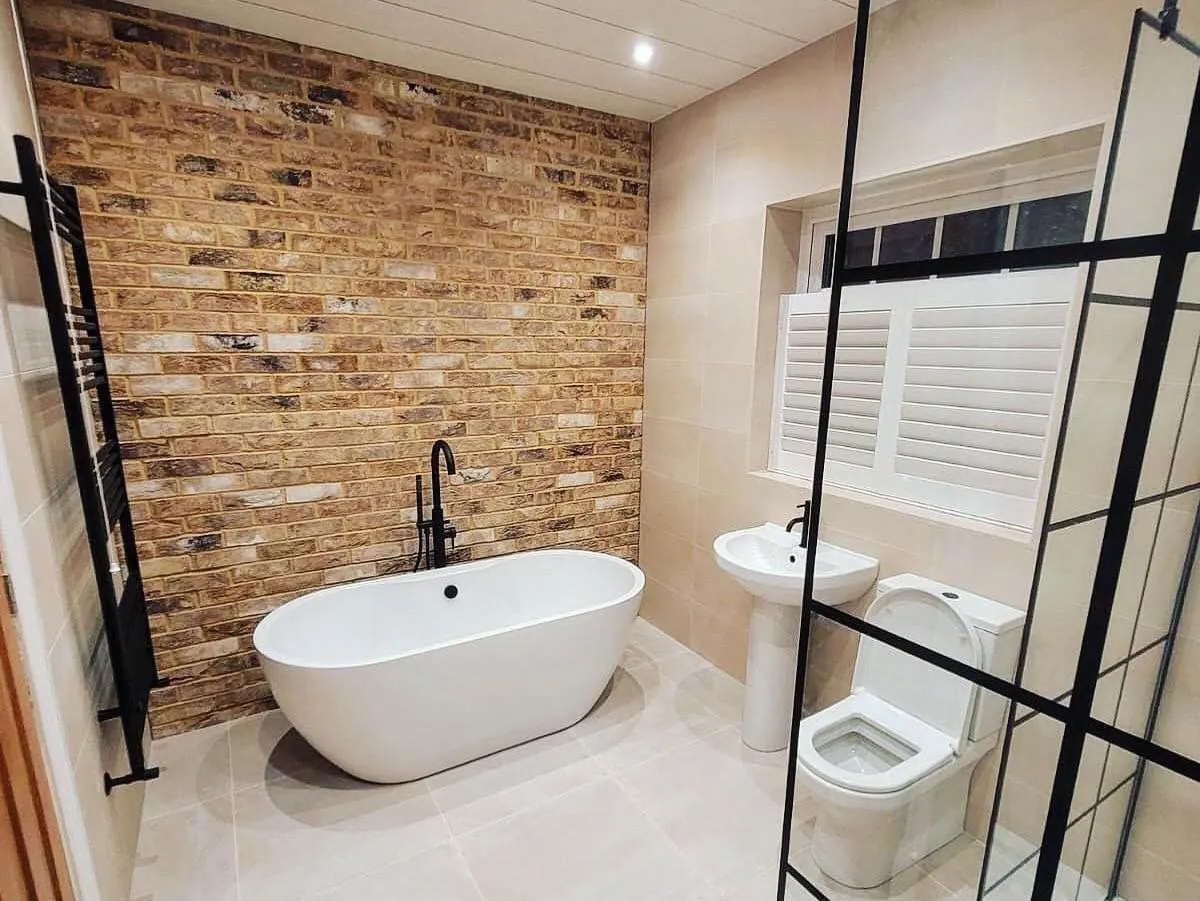 Warm brown brick slip bathroom feature wall behind a freestanding bath