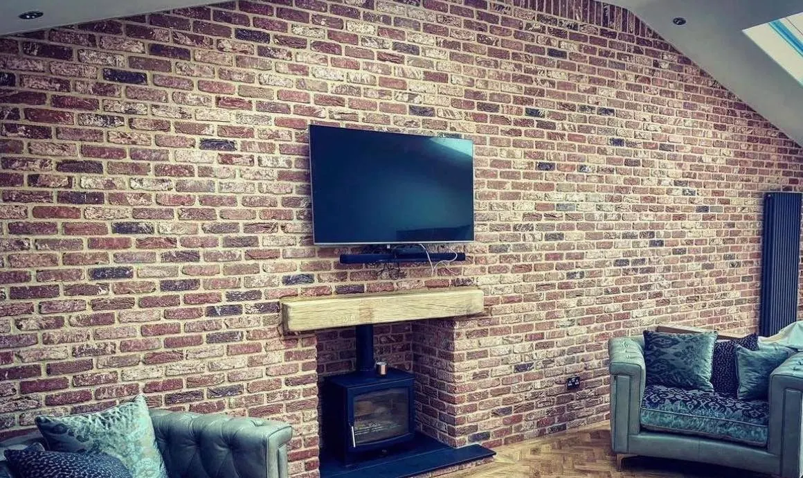 Brick slip feature wall in a living room with a TV and wood burner, fitted by Bespoke Brickwork