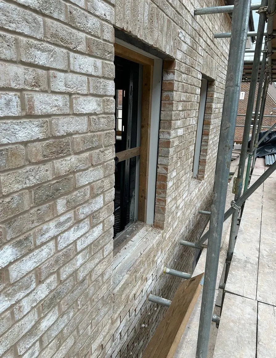 Pale brick slip cladding being installed around windows from scaffolding on a building