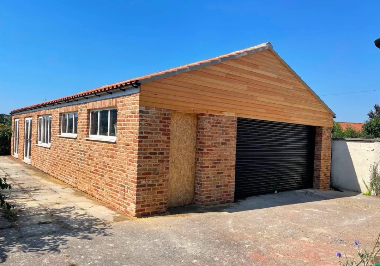 Red brick outbuilding with garage door and timber gable end