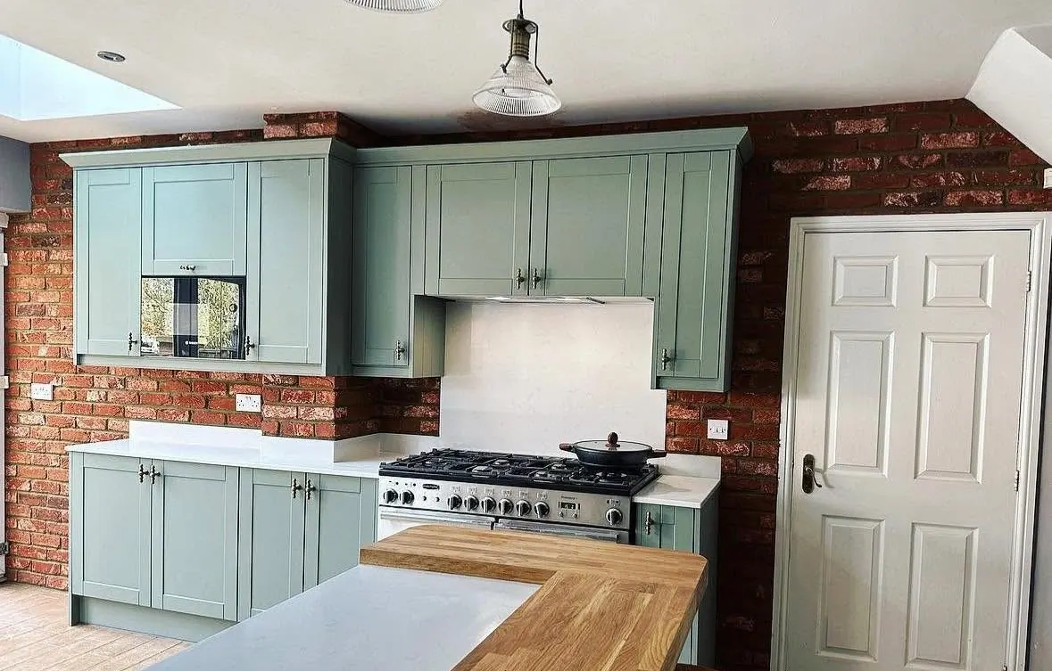 Red brick slip walls behind a pale green fitted kitchen